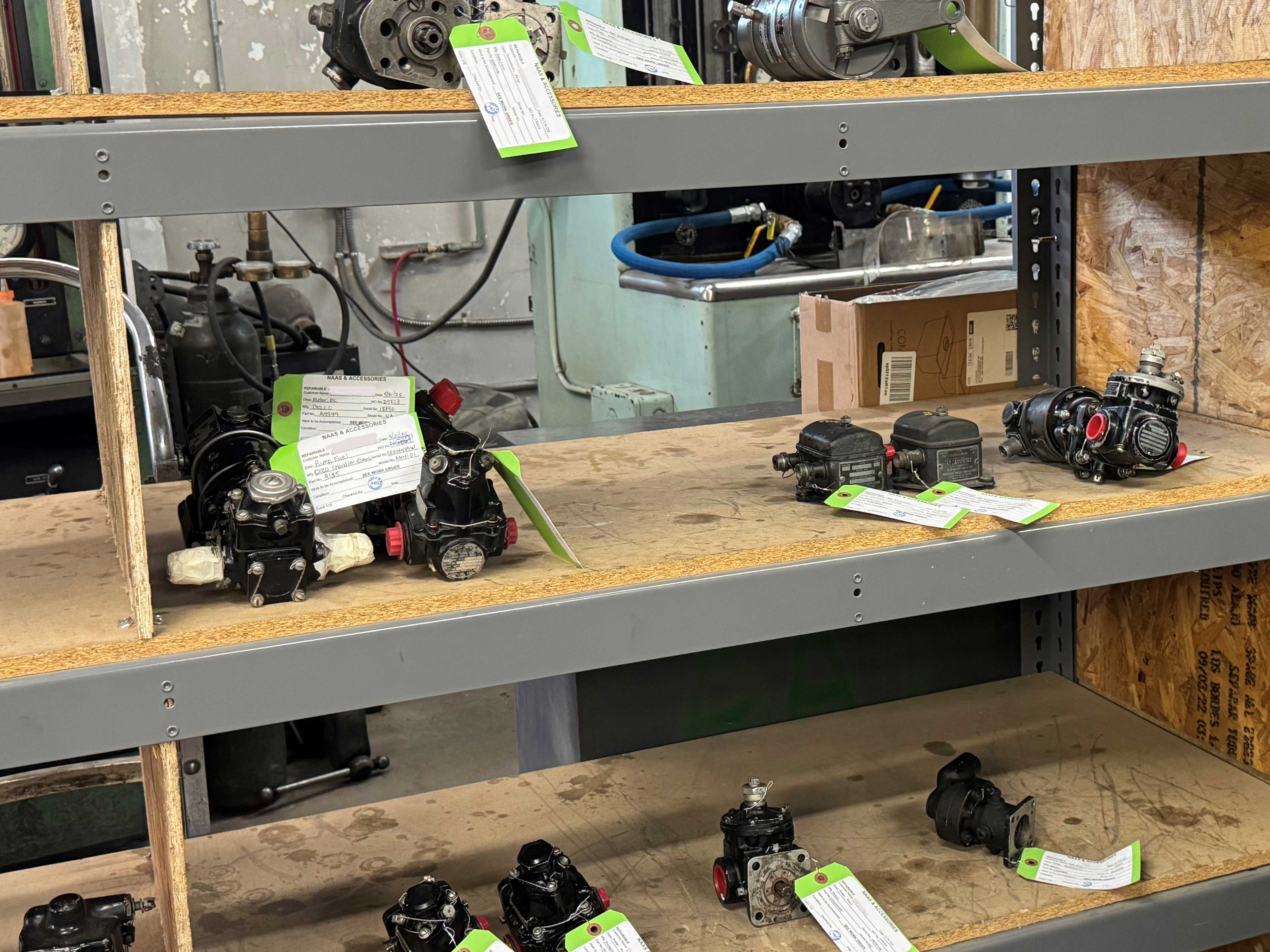 Multiple overhauled aircraft engine accessories with NAAS & Accessories inspection tags displayed on workshop shelving