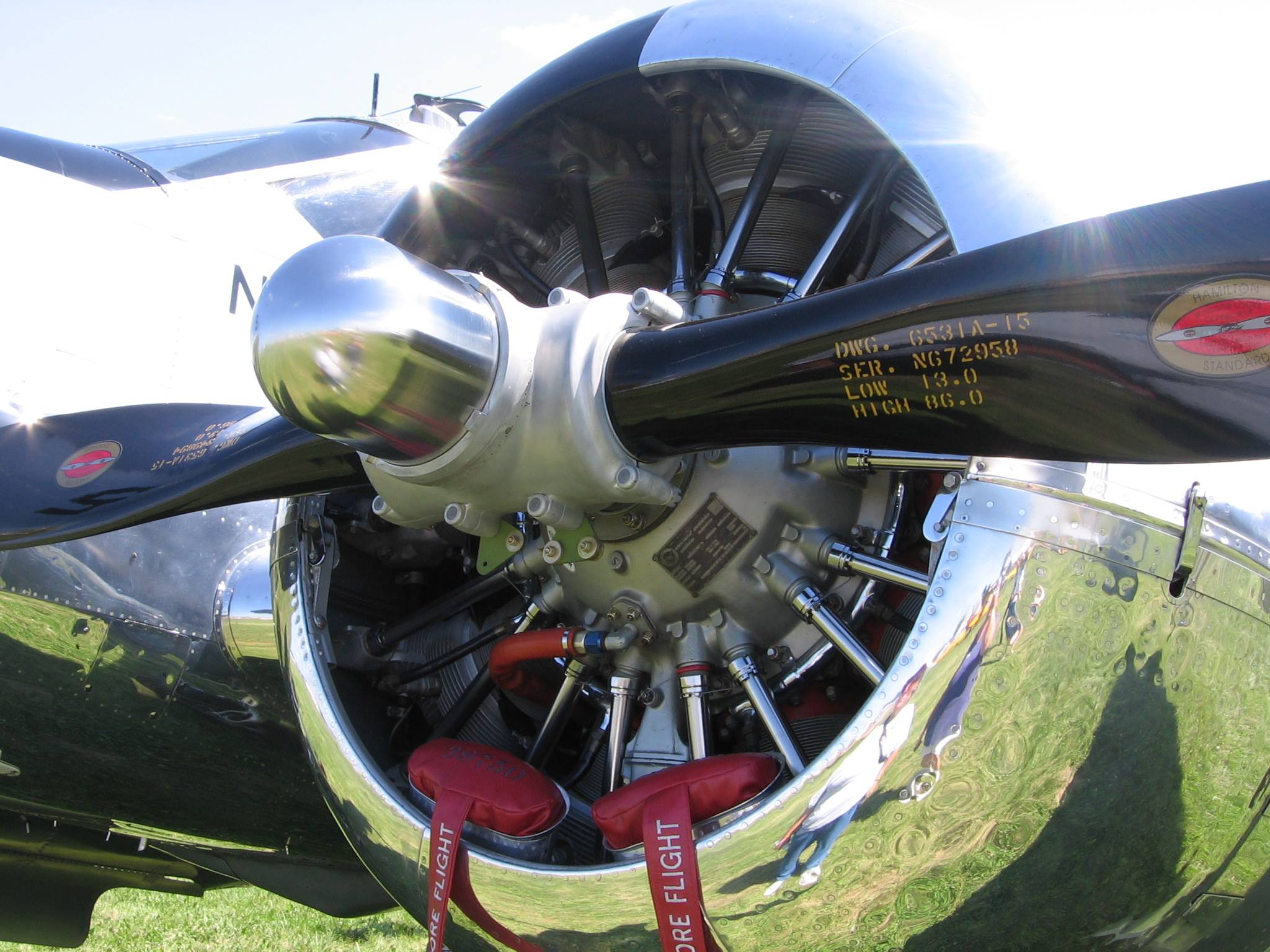 Close-up of an exposed polished radial aircraft engine and black propeller blade with red remove-before-flight valve covers, mounted on a grassy field