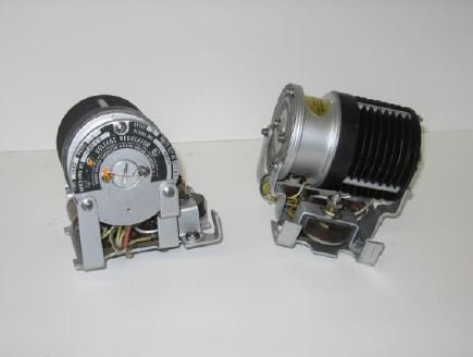 Two aircraft voltage regulators on a white background—one showing its adjustment dial and wiring, the other with a cylindrical body and black cooling fins