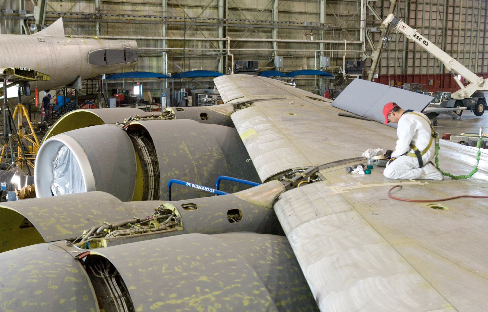 Aircraft in hangar under maintenance with technician inspecting fuel tank wing section