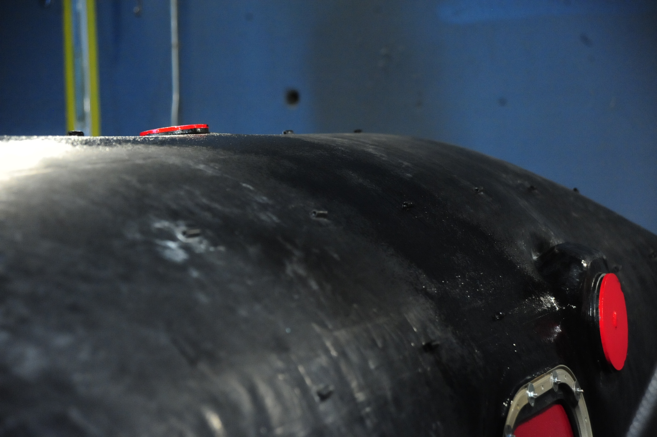 Close-up of a black aircraft integral tank section with red protective caps, showing surface repairs in a maintenance hangar