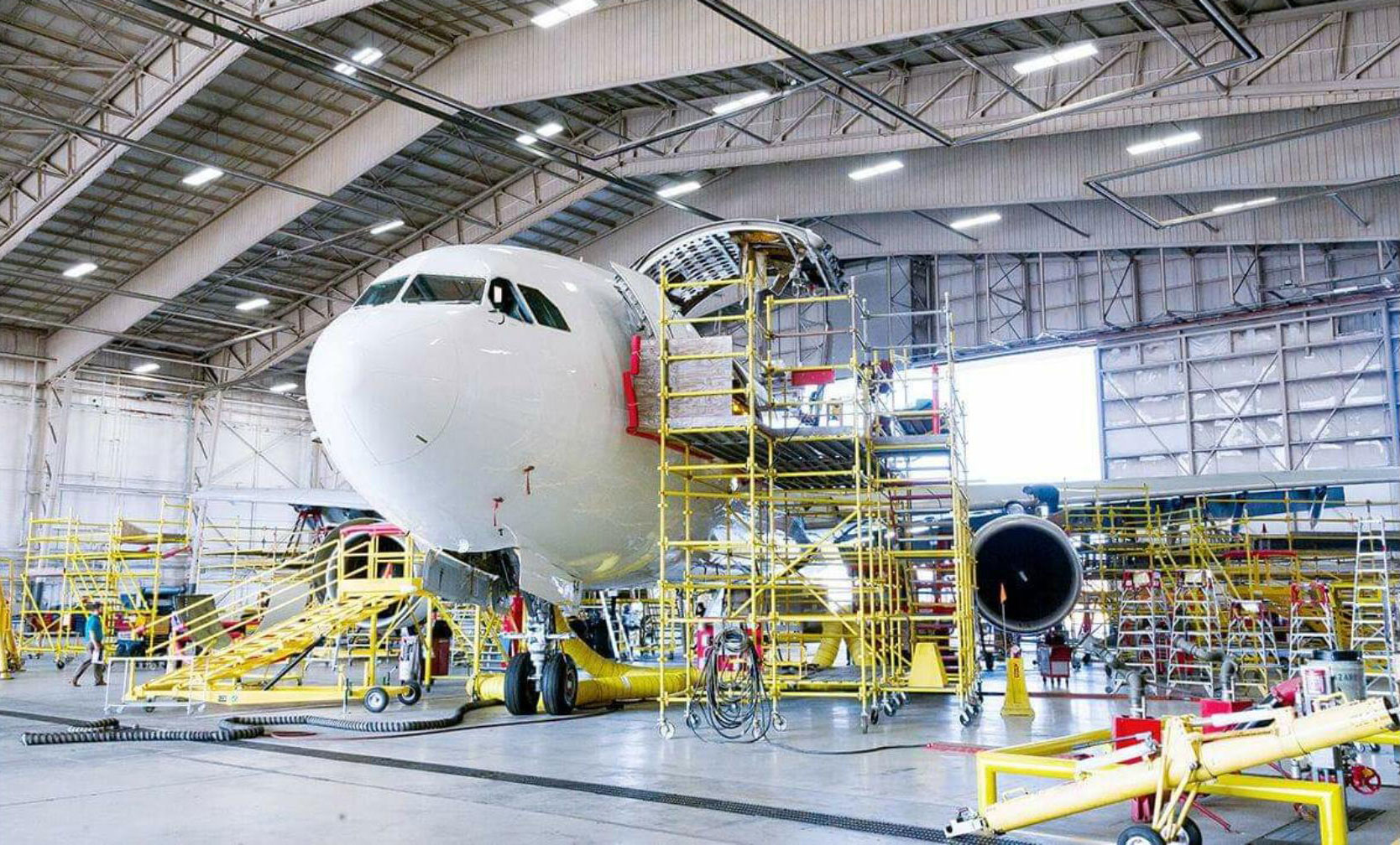 Commercial airliner nose inside an MRO hangar surrounded by yellow scaffolding and maintenance equipment for tailored maintenance programs