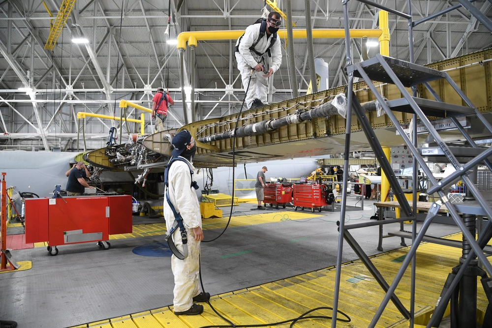 Technicians in protective coveralls performing expert onsite aircraft wing maintenance inside a hangar using mobile scaffolding