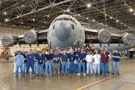 Group of NAAS & Accessories maintenance technicians and engineers standing in front of a large transport aircraft inside an MRO hangar